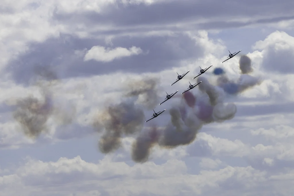 Six Patriots Jet Team L-39 Albatros jets approach the flight line in close formation, trailing dramatic smoke against a cloudy sky during SkyFest 2026 at Fairchild Air Force Base.